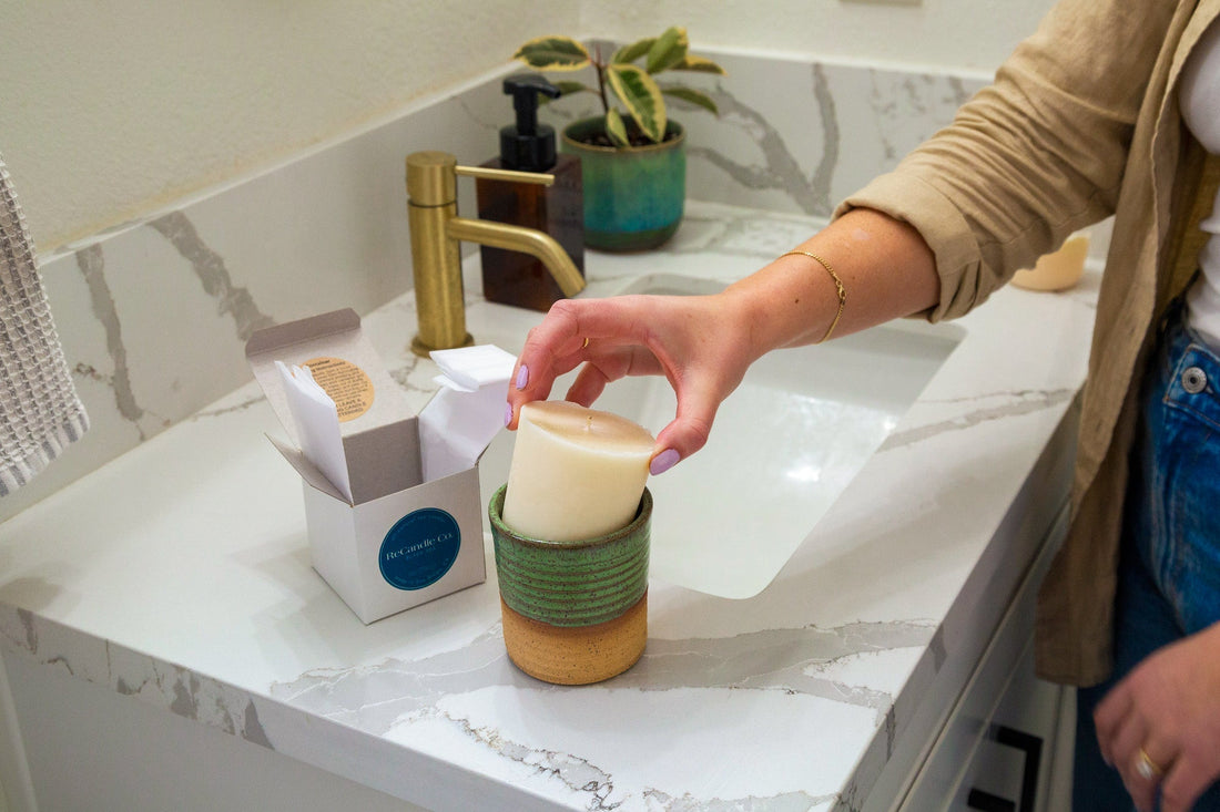 Person placing a ReCandle Co. soy wax refill into a handmade ceramic candle vessel on a bathroom counter.