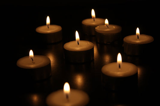 Tea light candles glowing in the dark, arranged on a smooth black surface. Soft, even flames ideal for tips on how to burn a candle evenly.