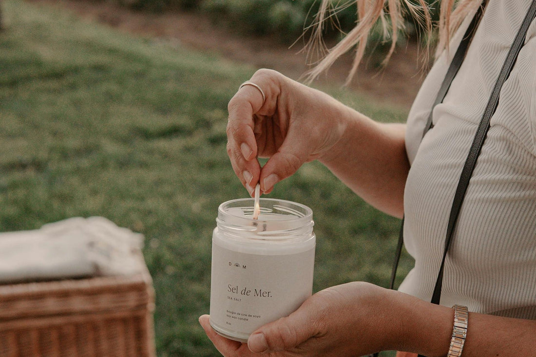 A person lighting a soy wax candle outdoors, capturing a peaceful moment that prompts the question: Are candles bad for the environment?