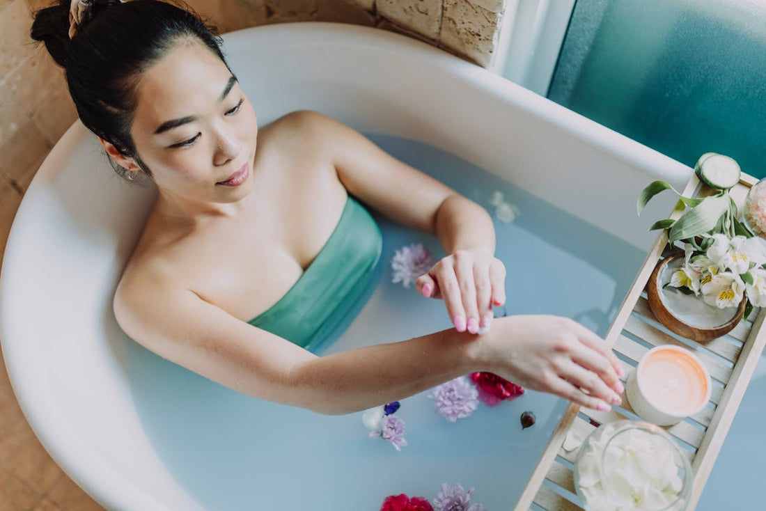 A woman enjoying a peaceful bath with flower petals and a lit candle nearby—highlighting one of the best candles for relaxation as part of a calming self-care routine.