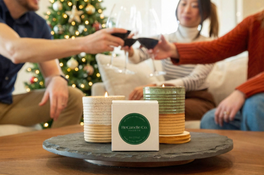 Friends toasting behind a lit Frasier Fir candle with a Christmas tree in the background.