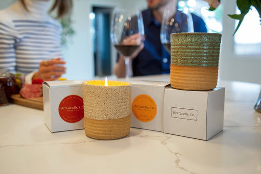 Couple enjoying wine with ReCandle Co.’s phthalate free candles on the table. Handmade ceramic vessels in warm tones shown with sustainable packaging.