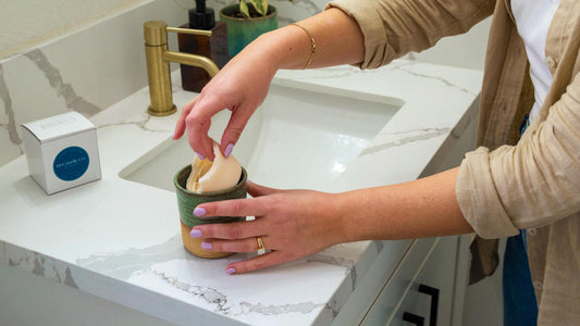 Person placing an eco-friendly candle refill into a reusable candle jar on a bathroom counter, demonstrating sustainable and waste-reducing options with ReCandle Co. products.