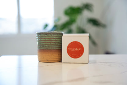 A teal colored ReCandle Co. ceramic candle vessel next to a ReCandle Co. 100% soy wax candle refill box.