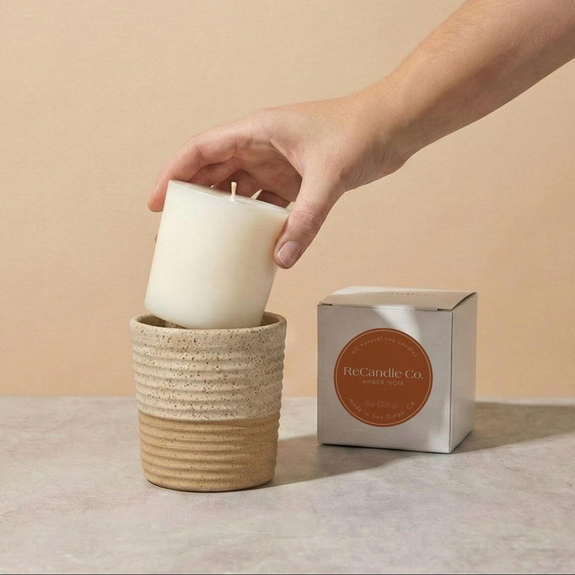 Person placing Amber Noir soy candle refill into walnut ceramic refillable candle holder