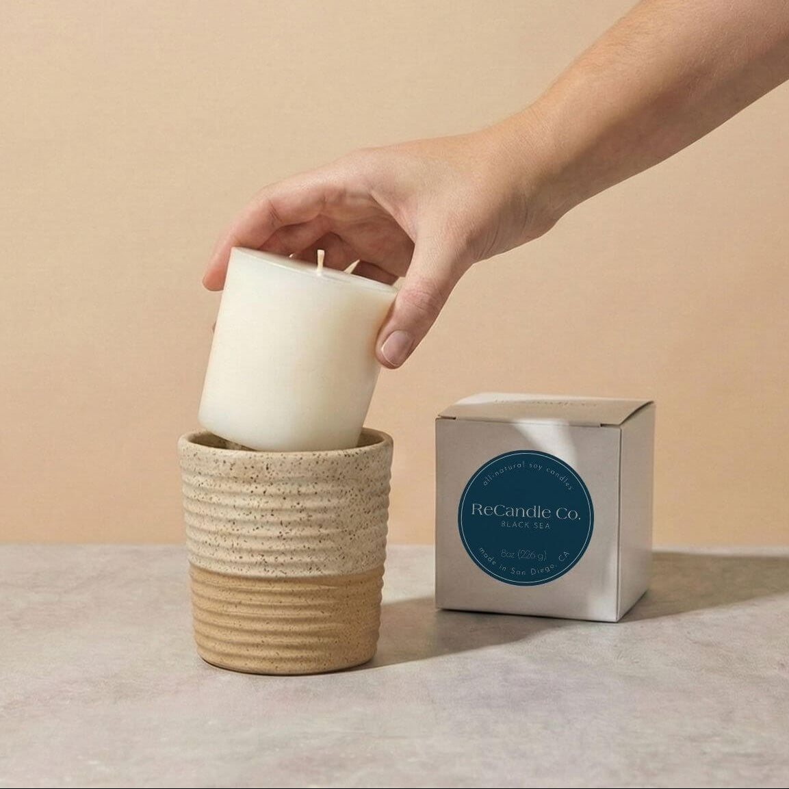 Person placing Black Sea soy candle refill into walnut ceramic refillable candle holder