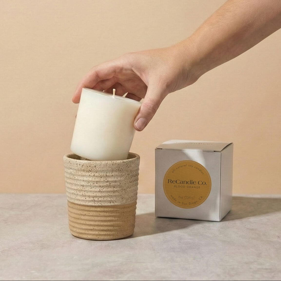 Person placing Blood Orange soy candle refill into walnut ceramic refillable candle holder
