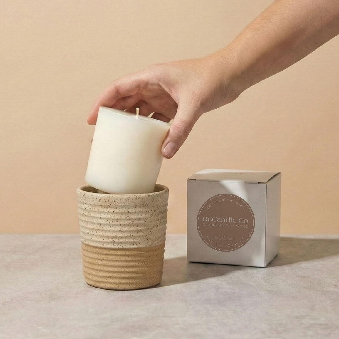 Person placing Caribbean Teakwood soy candle refill into walnut ceramic refillable candle holder