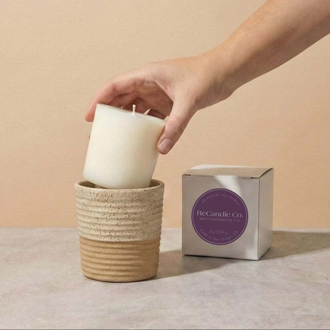 Person placing Mediterranean Fig soy candle refill into walnut ceramic refillable candle holder