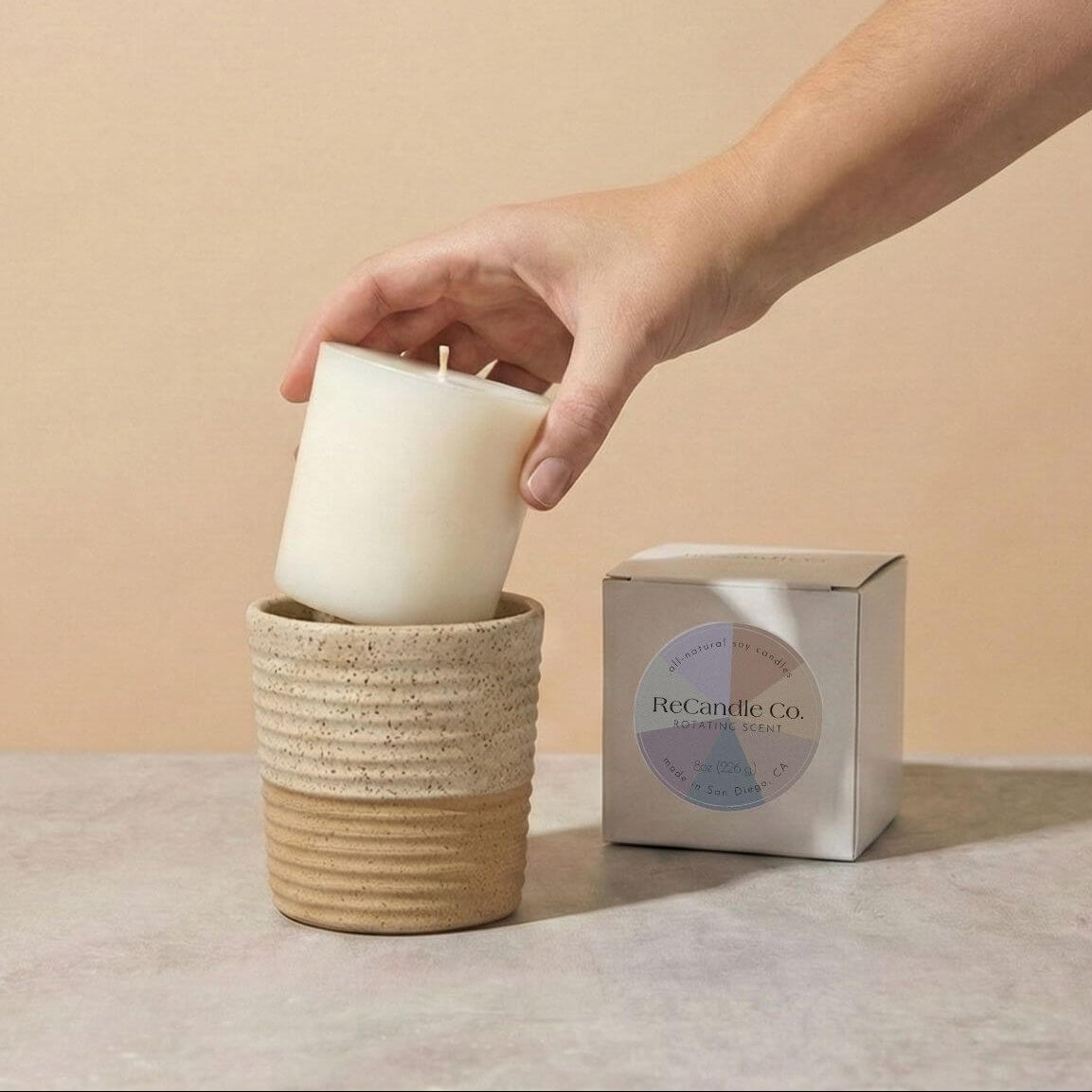 Person placing Rotating Scented soy candle refill into walnut ceramic refillable candle holder