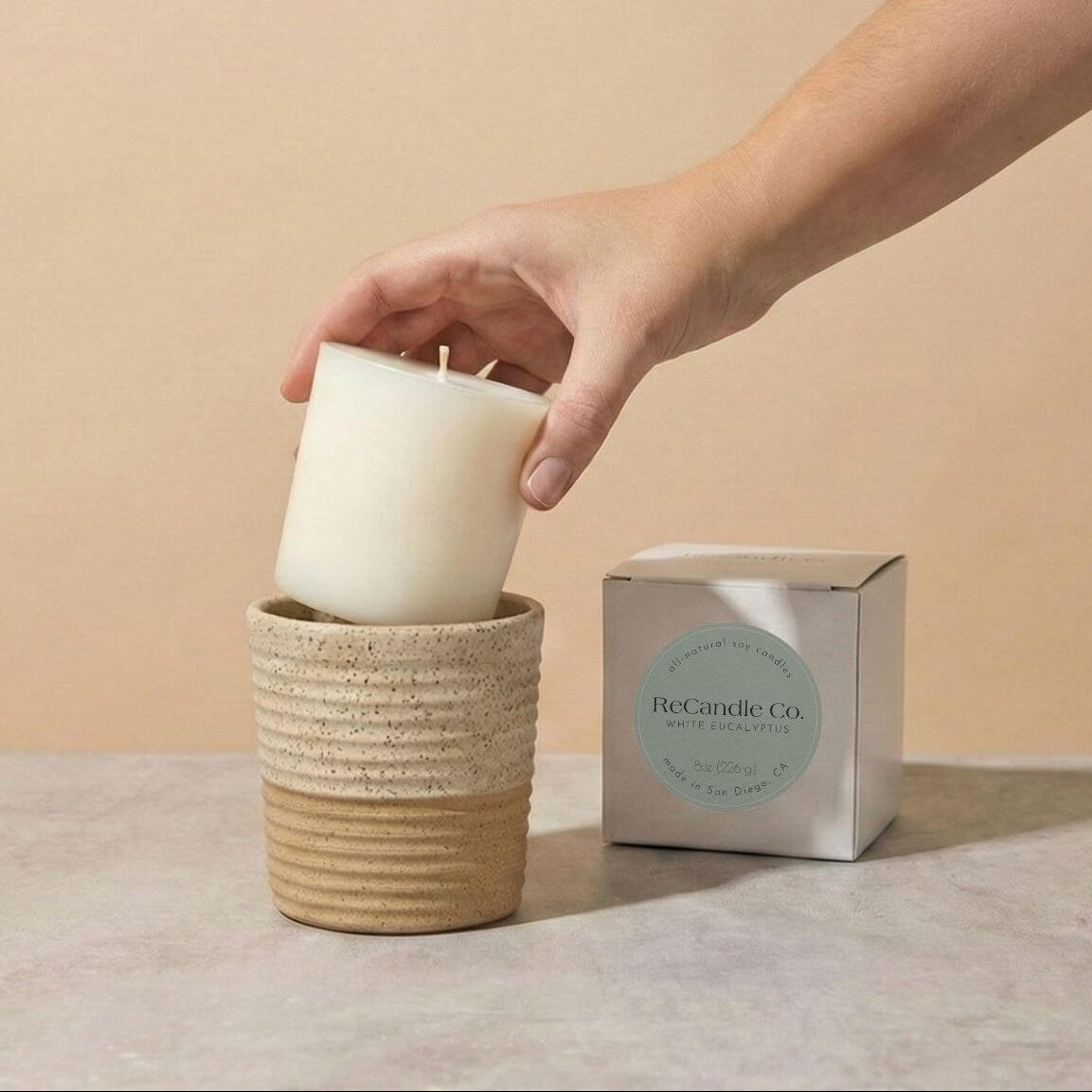 Person placing White Eucalyptus soy candle refill into walnut ceramic refillable candle holder